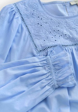 Hellblaue Bluse mit Blumenstickerei und Spitzendetails entlang des Halsausschnitts, mit gerafften Ärmeln und strukturiertem Stoff.