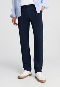 Pantaloni blu navy con una texture liscia, design a gamba dritta e passanti per cintura. Abbinati a una camicia azzurra e sneakers bianche.