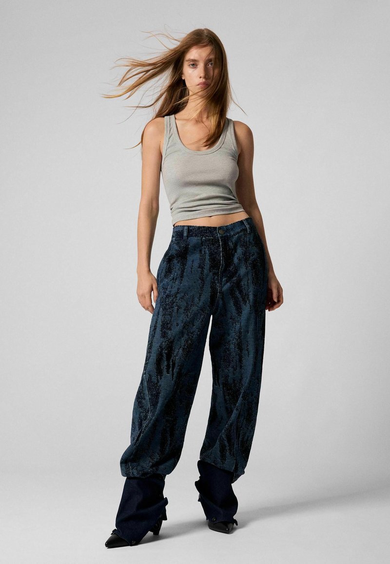 Hallatud hall tank top, millega on kombineeritud vabad tumehallid tekstuuriga püksid, millel on peen muster, ja mille lõpetuseks on terava ninaga mustad kontsad.