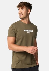 Olivgrünes Baumwoll-T-Shirt mit kurzen Ärmeln, verziert mit weißem grafischem Textdesign auf der Brust. Einfacher runder Halsausschnitt, lässige Passform.