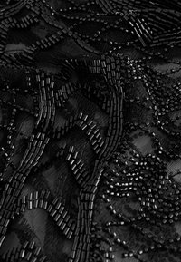 Mustmustekate kangas keeruka helkivate beedikujundustega, kus on läikivad mustad silindrilised ja ümmargused beedid. Pehme tekstuur koos kihiliste mustritega.