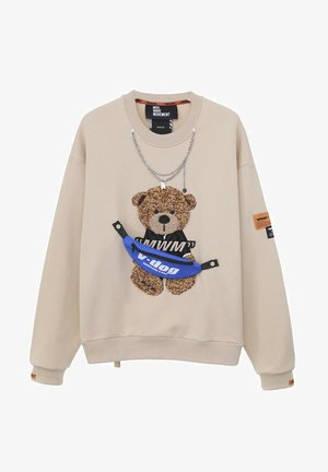 Sudadera beige con un gráfico de oso texturizado, cadenas superpuestas y una riñonera azul vibrante con el logotipo "v.dog". Incluye detalles y parches.