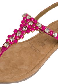 Sandalo piatto rosa con una fascia decorata da gemme rotonde rosa e trasparenti, su una soletta in suede beige.