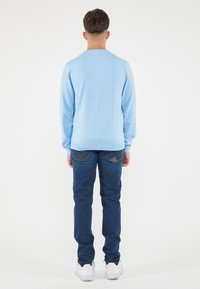 Maglione azzurro chiaro con maniche lunghe, abbinato a jeans blu scuro con dettagli cuciti sulle tasche e sneakers bianche.