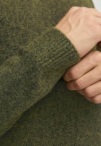 Olive green sweater with a textured knit design. The cuff features a ribbed pattern, emphasizing warmth and depth in color variation.