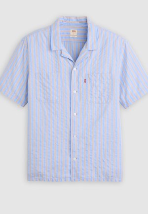 Chemise bleu clair à manches courtes avec boutons, rayures verticales blanches et beiges, deux poches poitrine et une petite étiquette rouge sur la poche gauche.