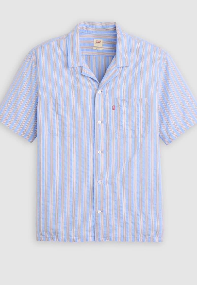 Camisa de manga corta azul claro con rayas verticales blancas y beige, dos bolsillos en el pecho y una pequeña etiqueta roja en el bolsillo izquierdo.