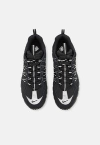 Pair of black and white Nike sneakers with textured soles, intricate lacing, and pull tabs, shown from top view on white background.