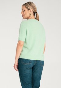 Miętowozielony sweter z krótkim rękawem, wykonany z miękkiego, teksturowanego materiału, z okrągłym dekoltem. Połączony z ciemnoniebieskimi dżinsami.