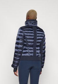 Tumedat sinine puhv jacket kõrge kraega, horisontaalselt tikitud paneelide ja kontrastsete tekstuuripaneelidega külgedel ja seljal.