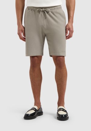 Lichtgrijze geribde shorts met een elastische tailleband en trekkoord. Bevat zijzakken en heeft een getailleerde pasvorm, gecombineerd met zwart-witte schoenen.