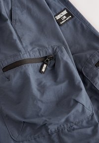 Giacca blu navy con tasca con cerniera e dettagli neri, completa di toppa con logo. Realizzata in materiale liscio e leggero.