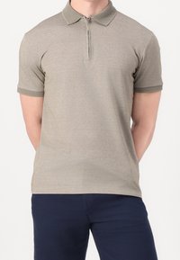 Polo en tissu gris clair avec un col texturé, des manches courtes, une fermeture éclair mi-longue et des accents en côtes au niveau du col et des poignets.