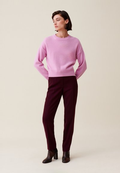 Pull en mélange de laine rose avec un col rond et des épaules tombantes, associé à un pantalon bordeaux slim-fit et des bottines à talons marron.