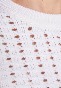 Pull blanc en tricot avec un motif ajouré comportant de petits trous et un col côtelé. Texture douce avec des accents marron contrastants.