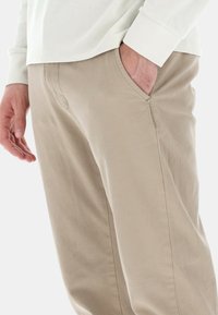 Pantaloni in cotone beige con taglio dritto, dotati di tasche laterali e dettagli di cucitura visibili. Texture morbida con un design pulito.