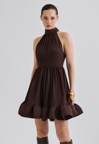 Brown, sleeveless halter dress with gathered neckline, fitted bodice, and flared hem featuring ruffled accents. Smooth fabric texture.