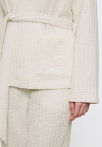 Set di loungewear trapuntato in crema, composto da un giubbotto con cintura e tasca a toppa e pantaloni abbinati, che presenta un motivo testurizzato.