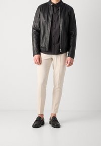 Svart läderjacka med ståkrage, matchad med en randig svart skjorta, gräddfärgade byxor och svarta loafers med tjocka sålar.