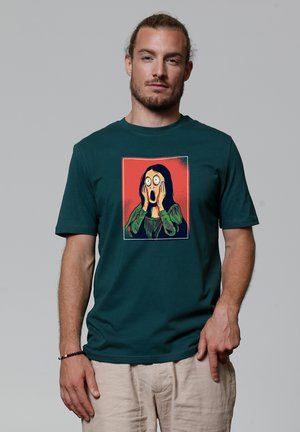 Teal cotton t-shirt featuring a printed illustration of a figure with hands on face, against a red background, showing wide eyes and long dark hair.