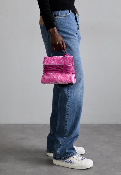 Piccola borsa a mano marmorizzata rosa con un design strutturato, dotata di manico superiore e diversi cinturini decorativi. Abbinata a jeans blu e scarpe bianche.