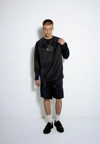 Czarny strój sportowy składający się z longslivowej koszulki i spodenek, z pionowymi paskami, błyszczącym logo oraz połączony z czarnymi butami i białymi skarpetkami.