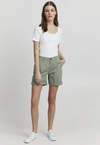 Haut à manches courtes blanc en rib avec un short vert à revers, doté d'un bouton à l'avant et de poches latérales. Baskets blanches.