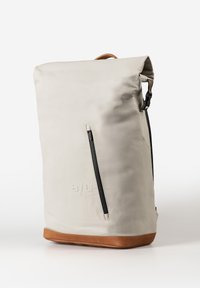 Packable backpack in light gray material with a roll-top design, black zipper closure, and brown leather base and accents.