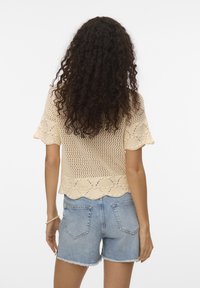 Haut en crochet beige à manches courtes, avec un ourlet en dentelle et un design en maille ouverte. Assorti à un short en denim bleu clair.
