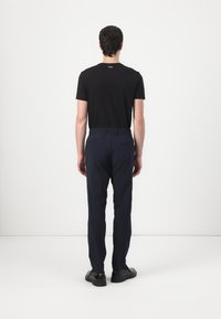Camiseta negra de manga corta con un logo en la parte de atrás, combinada con pantalones azul marino con cintura elástica y un bolsillo trasero, llevados con zapatos negros.