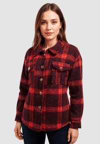 Chaqueta de cuadros rojos y oscuros con cuello de solapa, cierre de botones, dos bolsillos en el pecho y mangas largas. Fabricada con una tela texturizada.