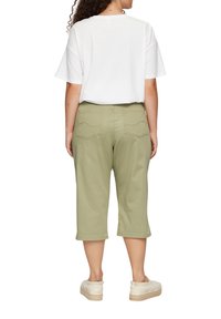 Pantalons verts olive à mi-mollet avec une coupe droite, deux poches arrière et des détails de couture subtils. Associés à un t-shirt blanc uni.