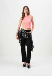 Top court rose vif, pantalon taille haute noir, chemise à carreaux nouée à la taille, sac à main noir et chaussures brillantes noires à bout pointu.