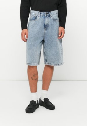 Light blue denim shorts with a loose fit, five pockets, and subtle fading. Worn with white socks and black slip-on shoes.