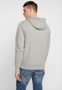 Grijze hoodie van een zachte, gestructureerde stof, verstelbare capuchon en ribbelmanchetten. Draagt met blauwe jeans, wat een casual uitstraling geeft.