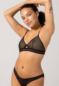 Svart mesh bralette med justerbara band, med en triangulär design, kontrasterande svart kant och en nyckelhålsöppning fram. Matchande svart mesh thongs.