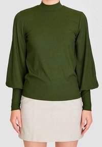Top de mangas largas de canalé verde oscuro con un cuello alto y mangas abullonadas, combinado con una mini falda beige claro con costuras frontales.