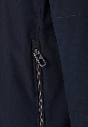 Metalen ritssluiting met een rechthoekige ritssluitingtrekker op donkerblauwe stof, met zichtbare stiksels langs de randen.