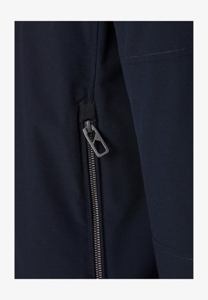 Metalen ritssluiting met een rechthoekige ritssluitingtrekker op donkerblauwe stof, met zichtbare stiksels langs de randen.