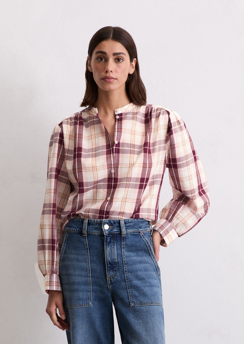 Chemise à manches longues à carreaux en crème, bordeaux et orange, avec un col mandarin et un bouton à l'avant. Portée avec un jean en denim taille haute.