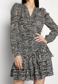 Vestido negro con lunares blancos, con mangas largas, escote en V y dobladillo con volantes en capas. Tela ligera y texturizada.