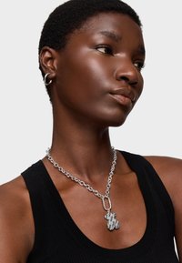 Collana in argento con pendente a forma di orso con testo inciso. Il modello indossa un top senza maniche nero, mettendo in evidenza la gioielleria.