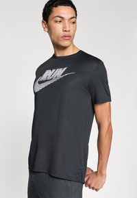 Čierne atletické tričko s krátkymi rukávmi a reflexným logom Nike. Materiál pôsobí hladko so slabým leskom.