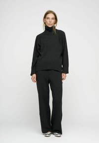 Mörkgrå, överdimensionerad turtleneck-tröja med ribbade ärmslut, i kombination med matchande vida byxor. Mjuk textur, minimalistisk design och inga synliga mönster.