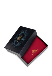 Tessuto rosso esposto all'interno di una scatola nera con elementi di design in oro e blu. Il tessuto ha un bordo seghettato con il nome del marchio "Wittchen."