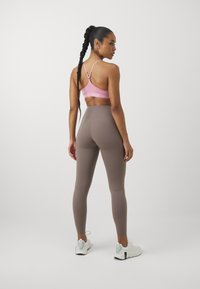Bruine leggings en een roze sportbh, met verstelbare straps. De leggings hebben een gladde textuur, terwijl de schoenen wit zijn met zwarte accenten.