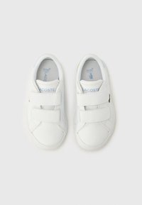 Λευκά αθλητικά παπούτσια με βέλκρο, με λείο συνθετικό επάνω μέρος, επενδεδυμένο γιακά και αεριζόμενη φόδρα, με μικρό πράσινο λογότυπο στο πλάι.