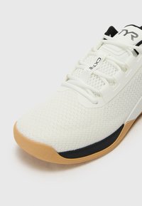 Baltie sporta apavi ar režģa augšu, gumijas zoli, melniem akcentiem un baltiem šņorēšanas virvēm, kurus bagātina "CXL2" birka pie mēles.