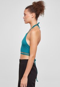 Teal ribbet halterneck crop-top med en tettsittende design, med tynne justerbare stropper og åpne sider, kombinert med svarte joggebukser med snøring.
