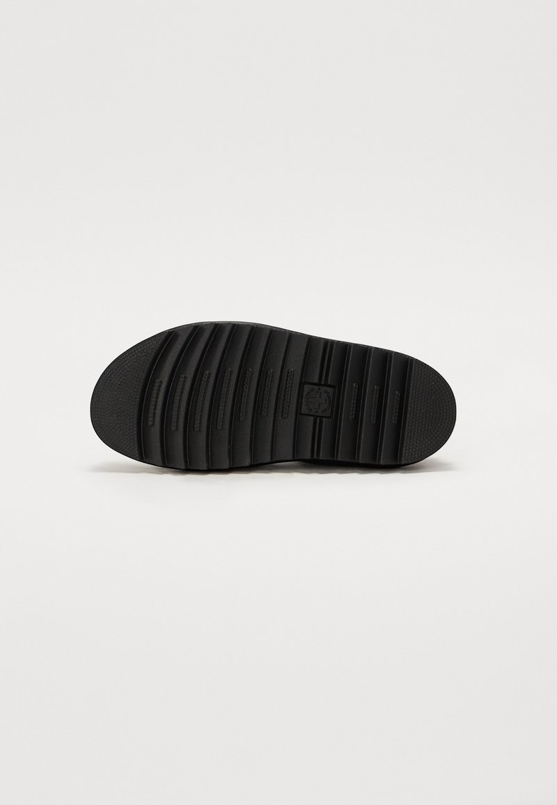 Schwarze Schuhsohle mit einem strukturierten, geriffelten Muster. Verfügt über ein zentrales Emblem mit Linien, die seitlich über die Oberfläche verlaufen, um Halt zu bieten.